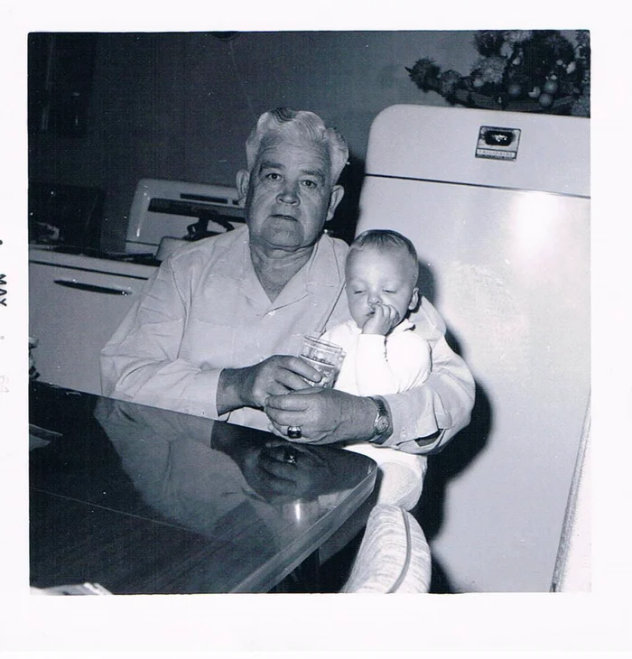 Aaron as a small child held by his grandfather Earl at a kitchen table, sharing a glass of water, photographed in May 1964