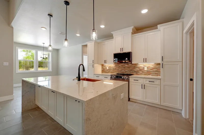 Kitchen island with stone countertop, pendant lights and a gas range along the back wall
