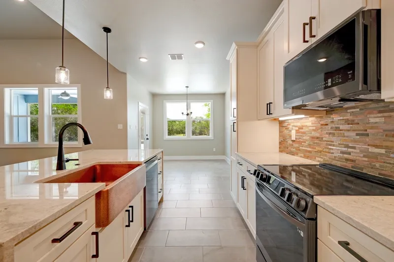 Copper apron sink in the island with the range and mosaic tile backsplash beyond