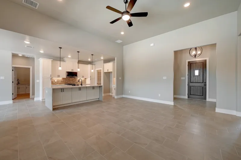Open living area under a vaulted ceiling looking through to the kitchen and front entry
