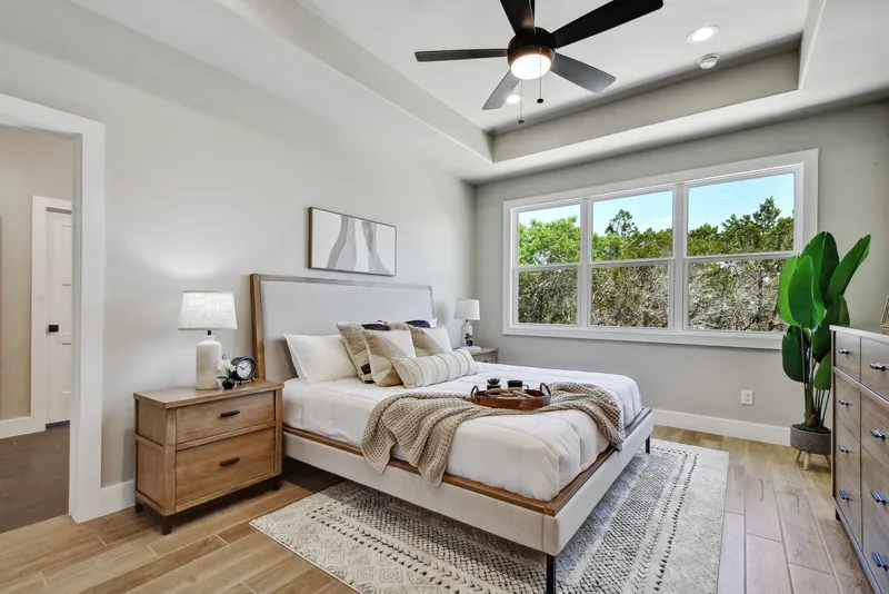 Primary bedroom with a tray ceiling and windows onto the tree line