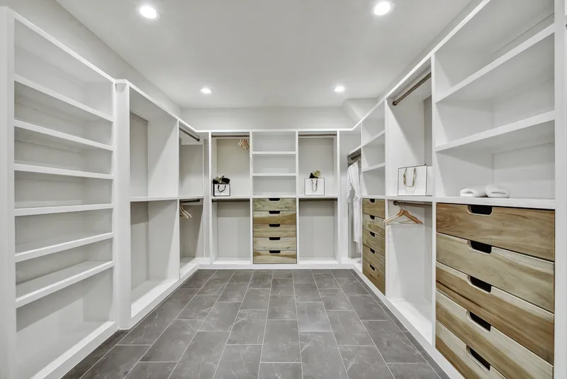 Walk-in closet with white built-in shelving on both walls and natural wood drawer banks
